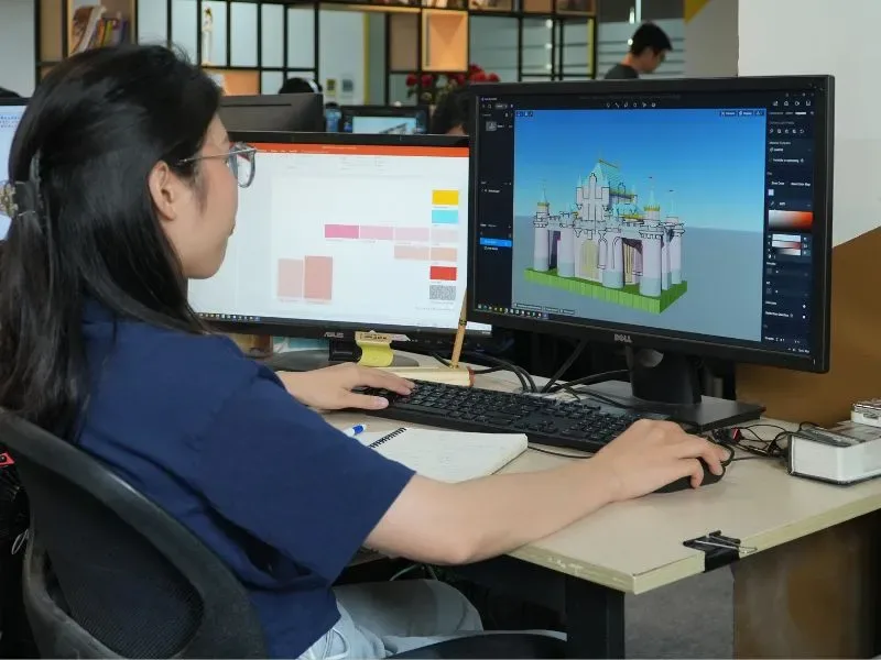 Người làm việc trước hai màn hình, một màn hình có hình lâu đài trong giao diện đồ họa