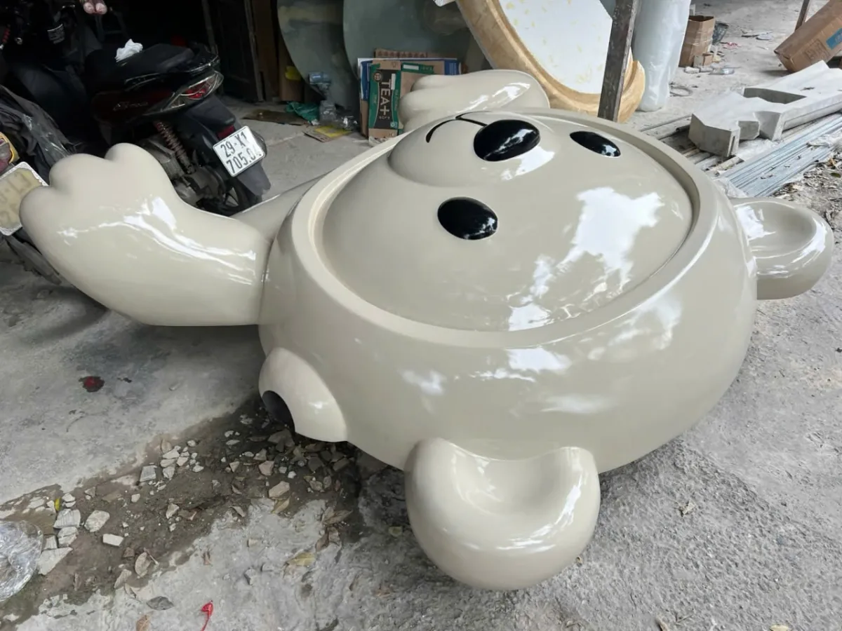 Mô hình nhân vật mặt tròn màu trắng đang đặt nằm trên sàn xưởng.