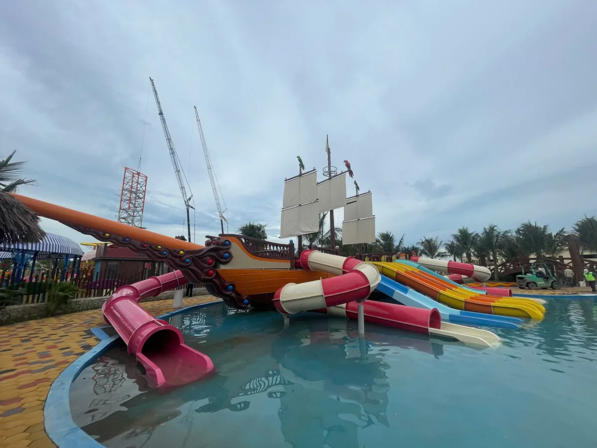 Mô hình tàu cướp biển composite lớn đặt trong hồ nước khu vui chơi resort, bao quanh là nhiều cầu trượt màu sắc và các...