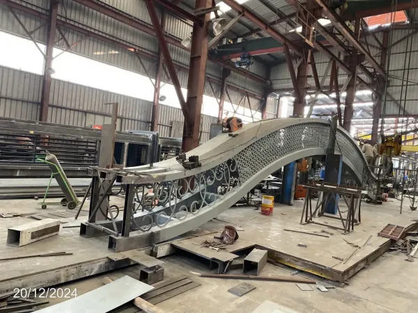 Nhịp vòm lớn có hoa văn uốn và tấm đục lỗ được kê trên giá trong xưởng