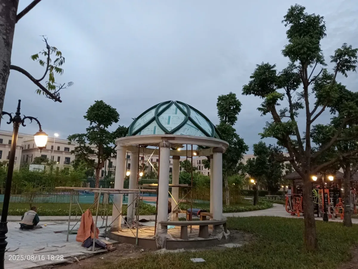 Chòi có mái vòm, các đường khung xanh và phần cột sáng màu giữa khuôn viên cây.