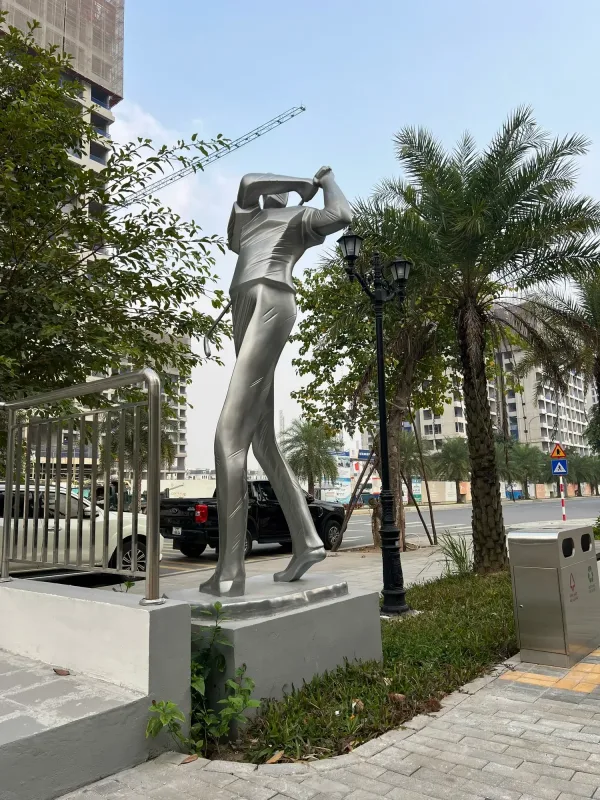 Tượng người chơi golf màu bạc đang vung gậy giữa cảnh quan khu phố
