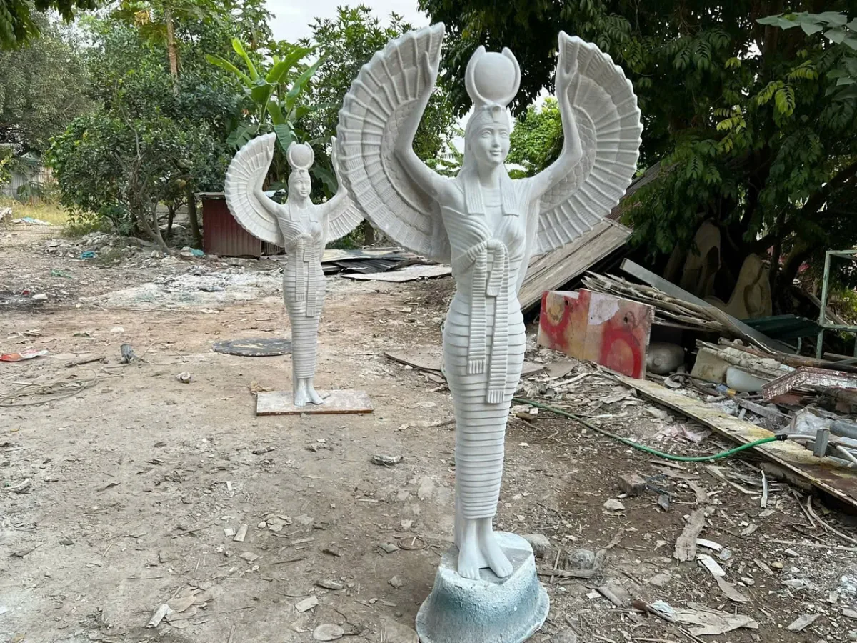 Hai tượng sáng màu dang đôi cánh, đặt ngoài trời giữa cây và vật liệu.