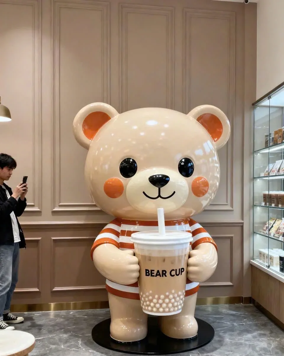 Gấu màu kem mặc áo sọc cam trắng, cầm cốc có chữ BEAR CUP