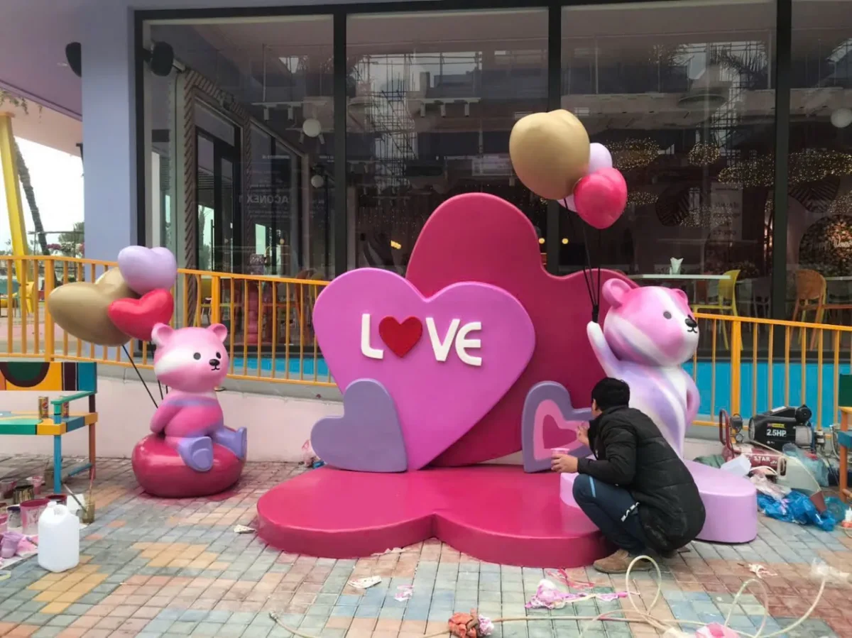 Tiểu cảnh trái tim hồng có chữ LOVE cách điệu và hai hình gấu trước cửa kính.